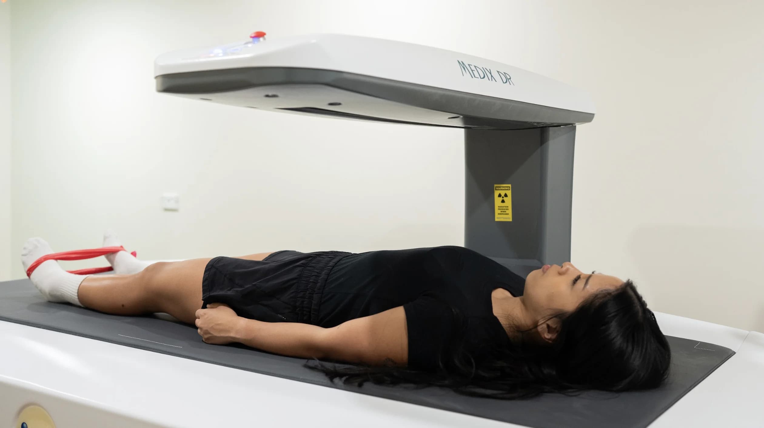 Patient lying still on the DEXA scanning bed as the scanner arm passes overhead
